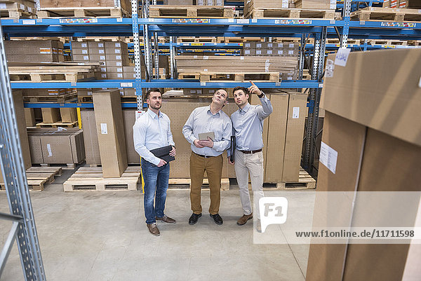 Three men with tablet talking in factory warehouse