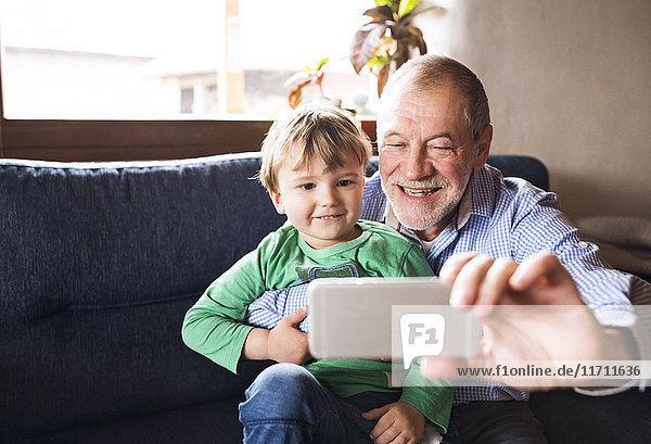 Großvater und Enkel sitzen auf der Couch und nehmen das Smartphone mit.