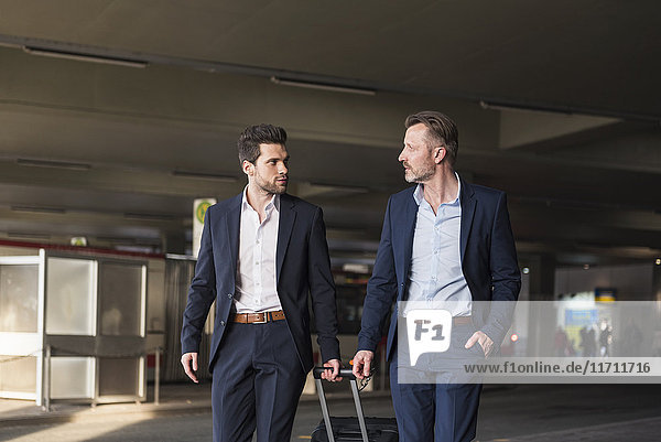 Two businessmen with rolling suitcase at bus terminal