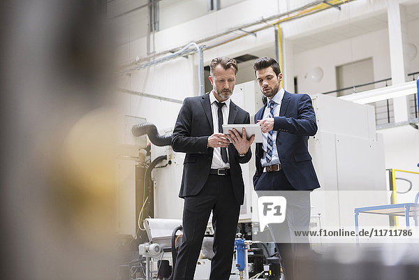Two businessmen sharing tablet in factory shop floor