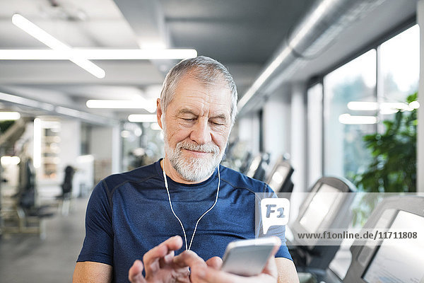 Senior man with smartphone and earphones in gym