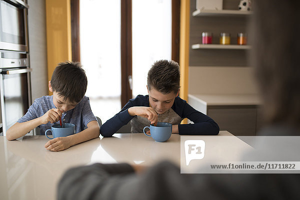 Two boys eating side by side at kitchen table