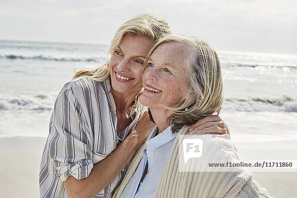 Senior woman and her adult daughter standing on the beach  embracing