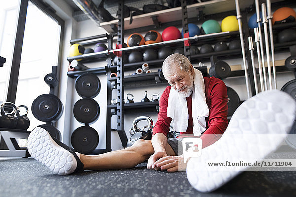Exhausted senior man sitting on the floor after working out in gym