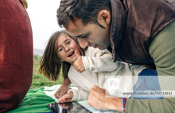 Glückliches Mädchen und ihr Vater benutzen Tabletten  die auf einer Decke im Freien liegen