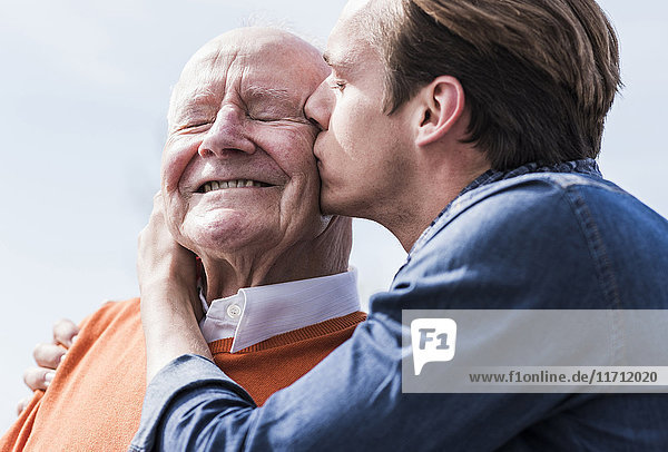 Adult grandson kissing senior man outdoors
