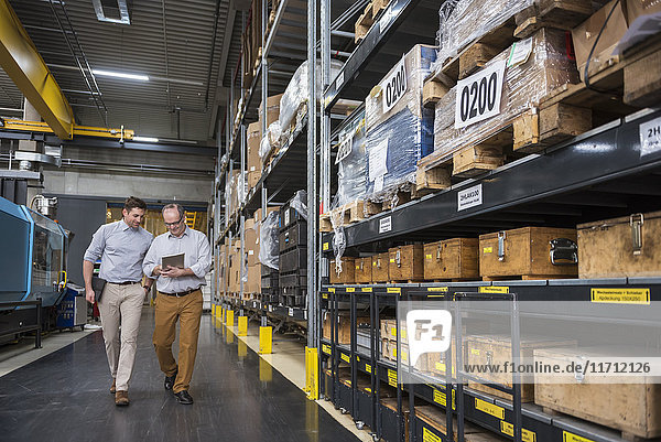 Two men with tablet walking in factory warehouse