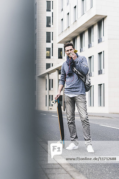 Geschäftsmann mit Skateboard  mit Smartphone und Kopfhörer