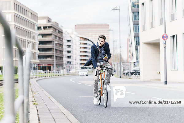 Businessman riding bicycle in the city  while using smartphone and earphones