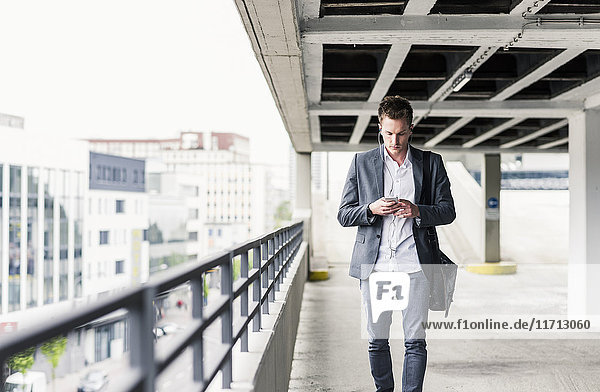 Young businessman using smartphone  walking on parking level