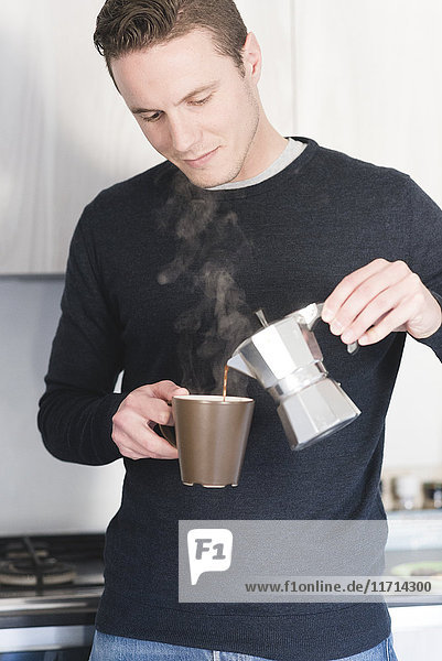 Mann gießt heißen Espresso in eine Tasse in der Küche