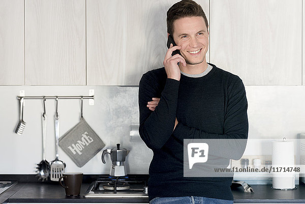 Porträt eines lächelnden Mannes am Telefon in der Küche