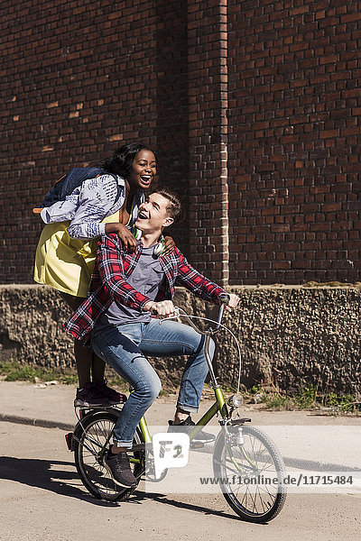 Junger Mann auf dem Fahrrad mit seiner Freundin auf dem Gestell stehend