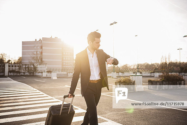 Businessman with rolling suitcase checking the time