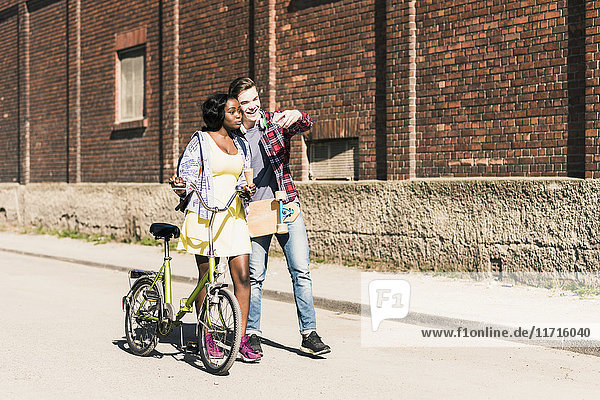 Junges Paar mit Fahrrad und Skateboard  das sich mit dem Smartphone auskennt