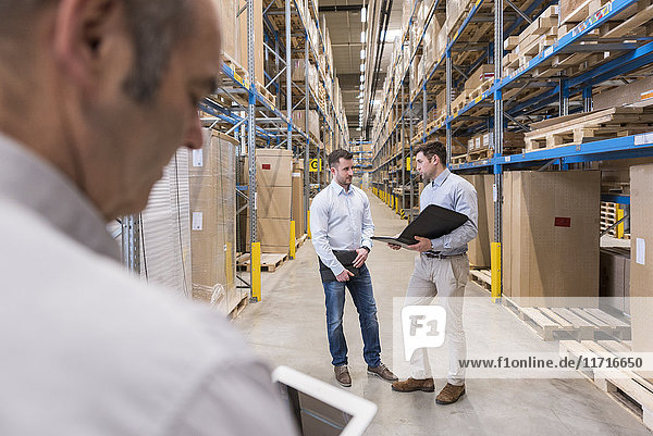 Two men with folder talking in factory warehouse