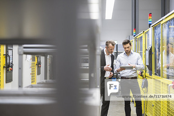 Two businessman observing industrial robots in factory