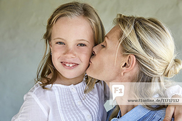 Porträt eines lächelnden kleinen Mädchens  das von seiner Mutter geküsst wurde.