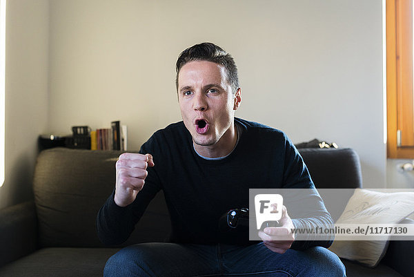 Porträt des schreienden Mannes auf der Couch mit Spielkonsole