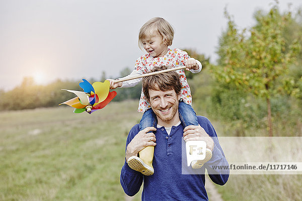 Father carrying daughter with pinwheel on shoulders