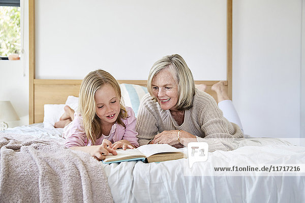 Kleines Mädchen auf dem Bett liegend mit ihrer Großmutter  die ein Buch liest.
