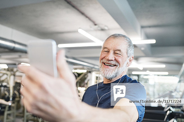 Glücklicher Senior mit Smartphone und Kopfhörer im Fitnessstudio