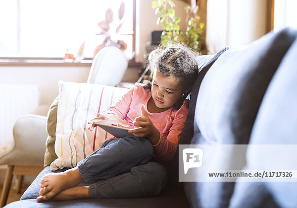 Little girl using sitting tablet  sitting on couch
