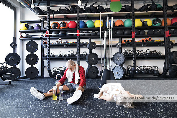 Exhausted senior couple recovering on the floor after working out in gym