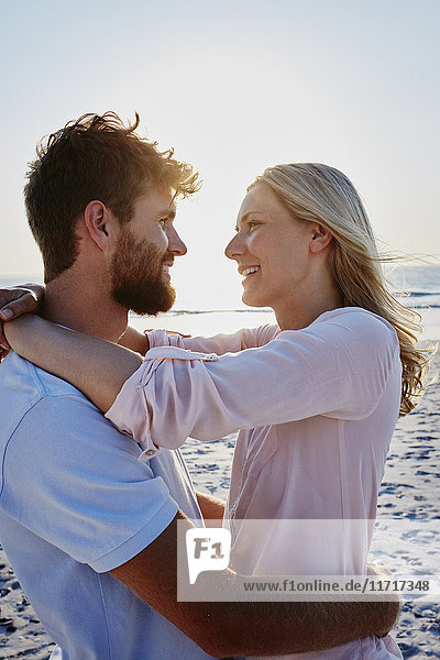 Lächelndes Paar  das sich bei Sonnenuntergang am Strand umarmt.