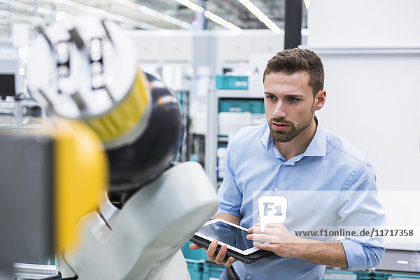 Man with tablet examining assembly robot in factory shop floor