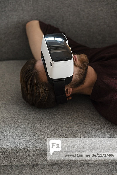 Man lying on the couch using Virtual Reality Glasses