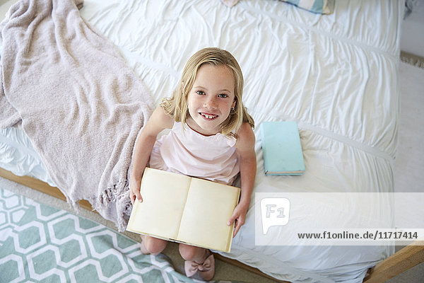 Porträt eines kleinen Mädchens auf dem Bett sitzend mit Buch