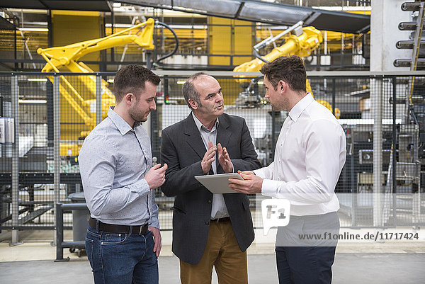 Three men with tablet talking in factory shop floor