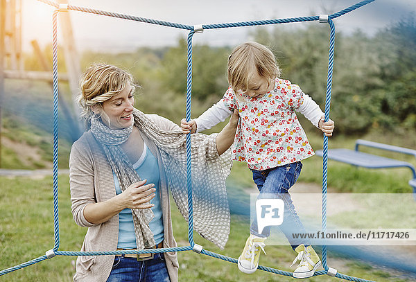 Girl on playground in climbing net supported by mother