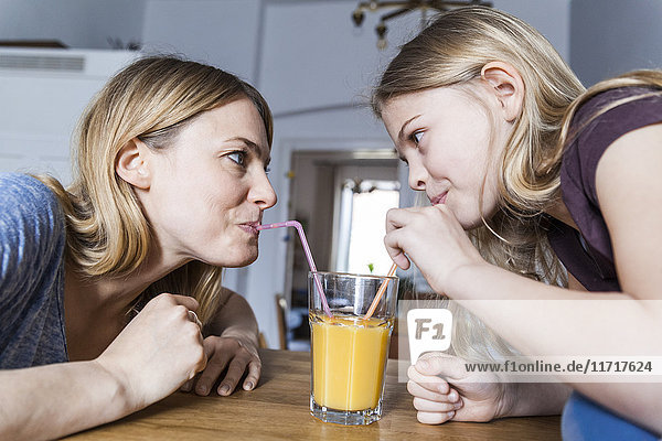 Mutter und Tochter teilen sich einen Orangensaft in der Küche.