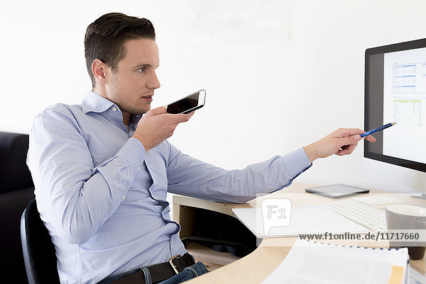 Businessman with smartphone looking at computer screen