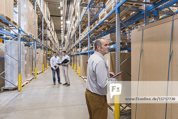 Man with tablet and two men with folder in factory warehouse