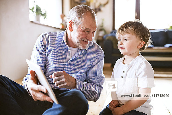 Großvater und Enkel auf dem Boden sitzend  mit digitalem Tablett