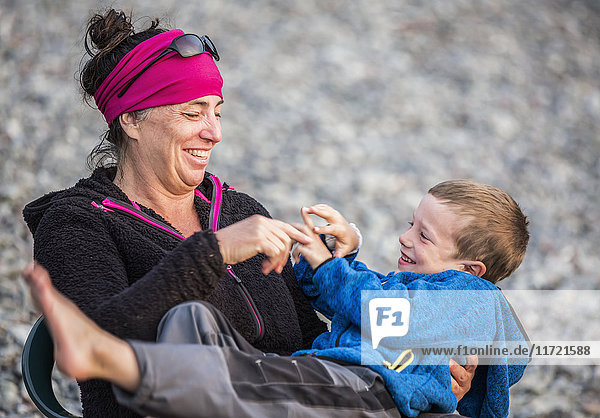 Eine Mutter spielt mit ihrem Sohn  während sie sich in einem Stuhl am Ufer von Hesketh Island  Süd-Zentral-Alaska  USA  entspannt.