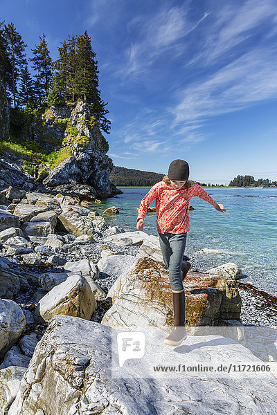 Young girl plays on rocks along the shore near Seldovia  Southcentral Alaska  USA
