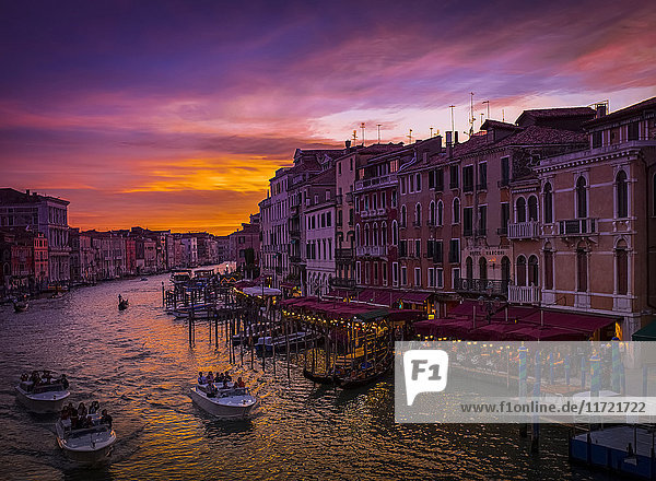 Ein dramatischer und farbenfroher Sonnenuntergang über dem Kanal und den Gebäuden  mit Wassertaxis im Kanal; Venedig  Italien'.