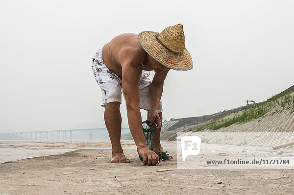 'A fisherman working with his net to get some small fish in Yangtze river; Chongqing China'
