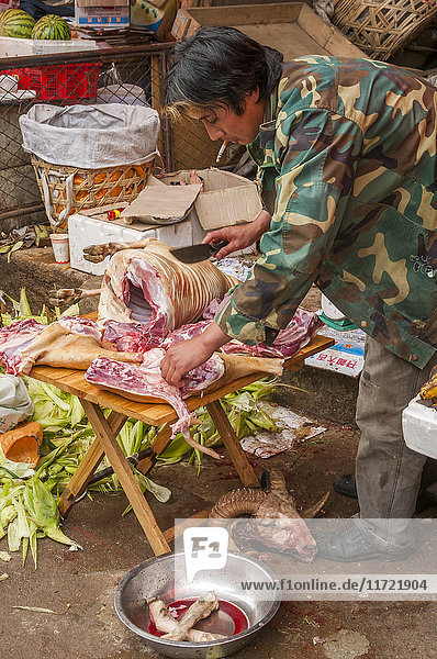 'A vendor prepares meat to sell in this market where we can see people from different minority groups and the daily life of Famous Shangrila village; Shangrila Yunnan province China'