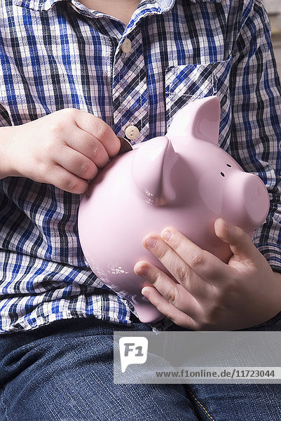 Junger Junge,  der Münzen in ein Sparschwein einzahlt; Laval,  Quebec,  Kanada