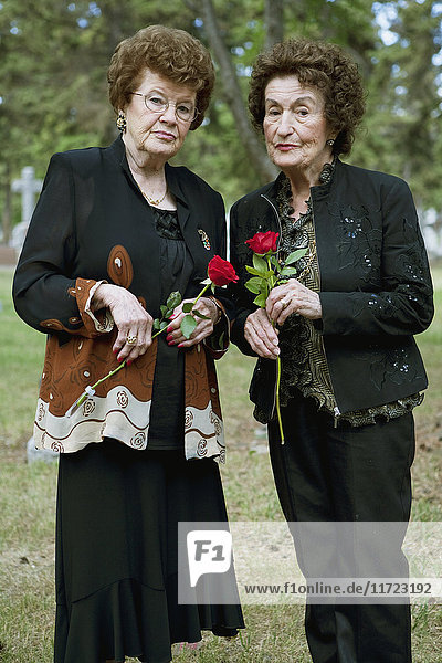 Zwei Frauen halten einzelne rote Rosen auf einem Friedhof; Edmonton  Alberta  Kanada'.