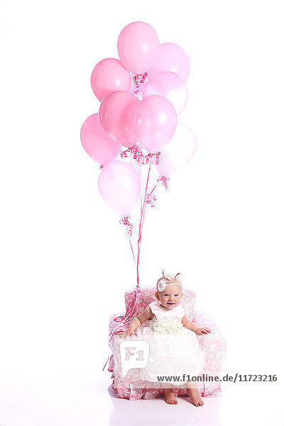 'Portrait of a young girl in a white dress sitting in a pink chair with a bouquet of pink balloons; Oregon  United States of America'