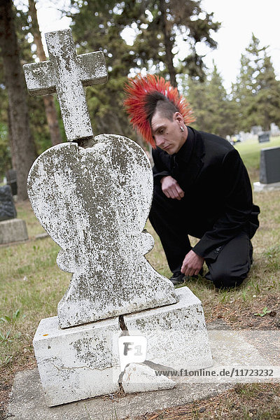 Ein junger Mann mit rotem Irokesenschnitt trauert um einen Grabstein auf einem Friedhof; Edmonton  Alberta  Kanada'.
