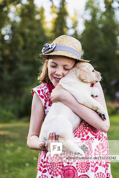 'A young girl wearing a sundress and hat holding a Labrador puppy in her arms; Anchorage  Alaska  United States of America'