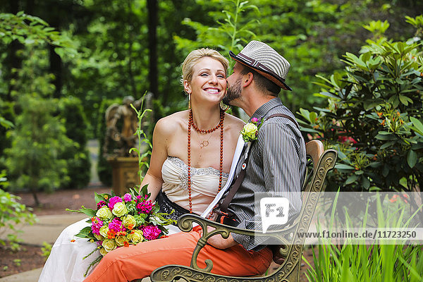 'A bride and groom sit on a bench in a garden; Oregon  United States of America'