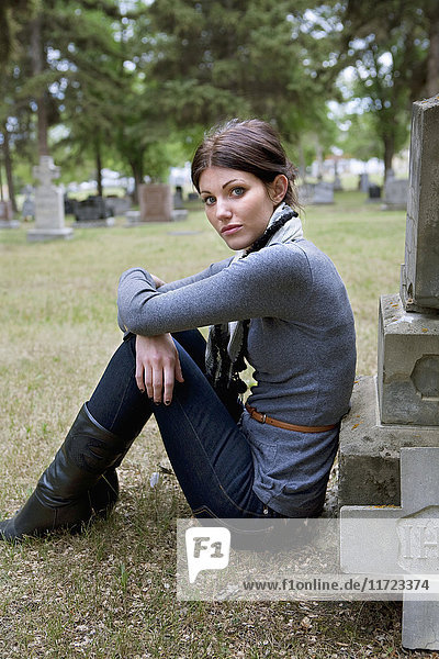 Eine junge Frau sitzt an einem Grabstein auf einem Friedhof; Edmonton  Alberta  Kanada